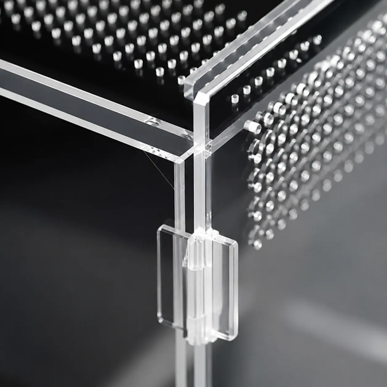 Macro close-up of a top corner of the clear acrylic enclosure showing the joined panel seam, rows of drilled ventilation holes and a clear plastic locking clip, against a dark background