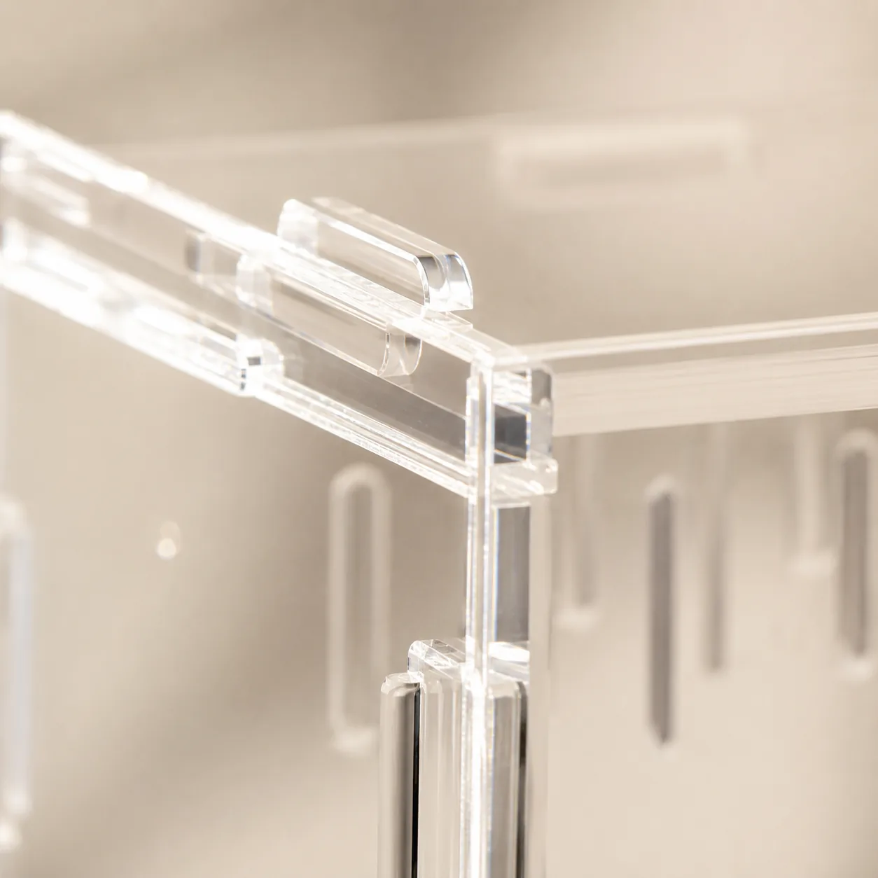 Close-up of the top corner of the clear acrylic enclosure, showing the transparent hinge tab of the lid and the laser-cut ventilation slots on the side panel